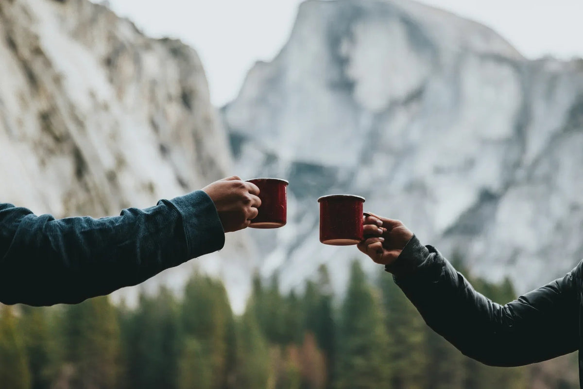 Two people holding red mugs in front of a mountainous landscape