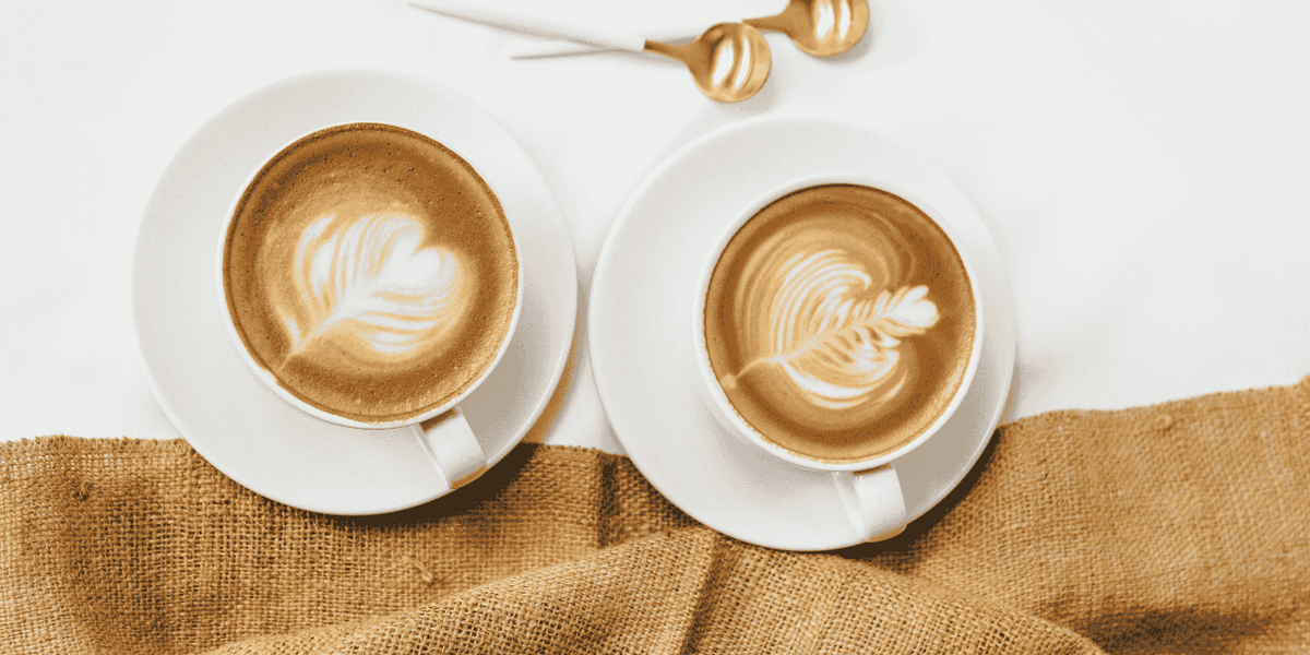 Two cups of mannabrew with latte art on a white surface with a burlap napkin.