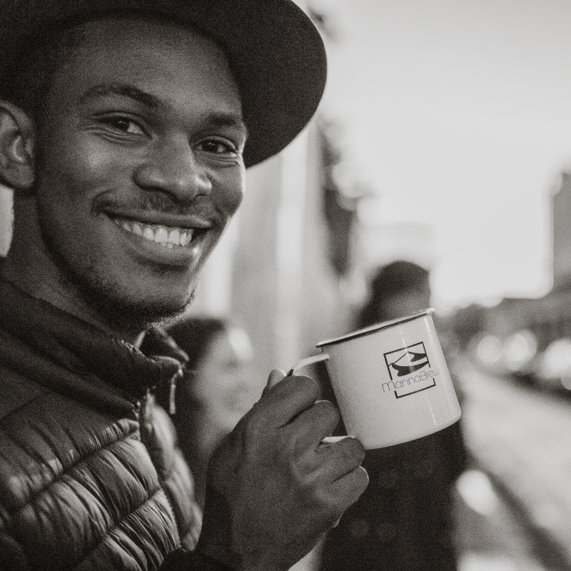 Man holding a mug with the mannabrew logo, smiling outdoors